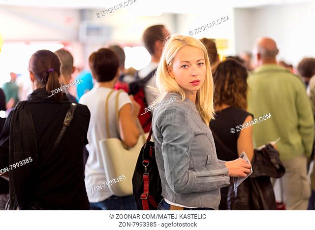 Young blond caucsian woman waiting in line with plain ticket in her hands. Lady standing in a long queue to board a plane
