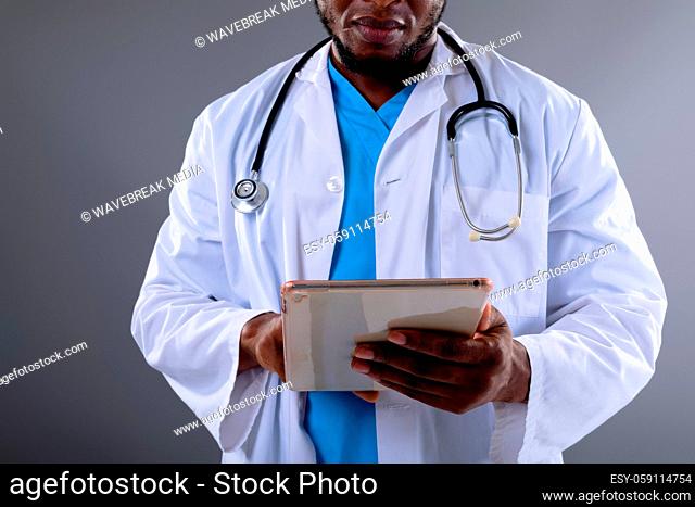Mid section of african american male doctor using digital tablet against grey background