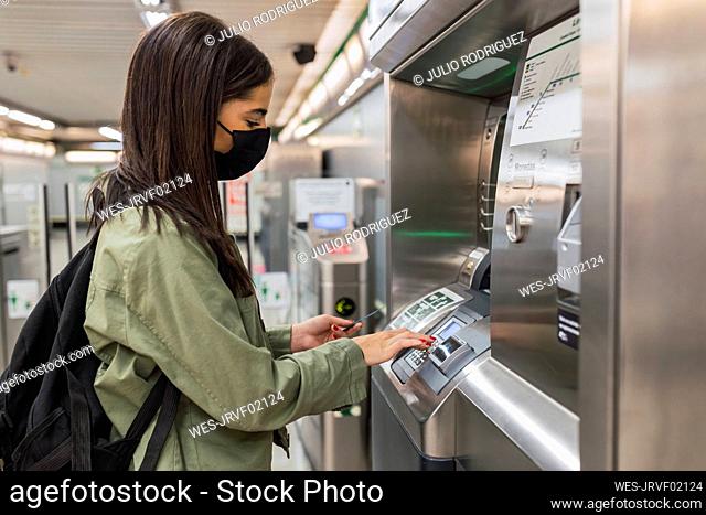 Young woman wearing face mask using ticket machine