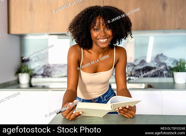 Afro woman with book leaning on kitchen island at home