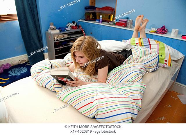 14 year old Teenage girl reading a book lying on the bed in her bedroom