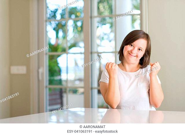 Down syndrome woman at home very happy and excited doing winner gesture with arms raised, smiling and screaming for success. Celebration concept