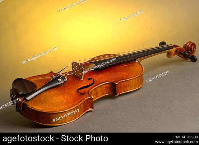 An old violin with slight scratches and damage lies on a neutral, gray, yellow-lit background. | usage worldwide. - /Deutschland