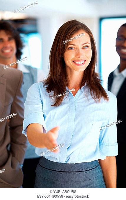 Beautiful business woman offering you handshake with multi ethnic team in background