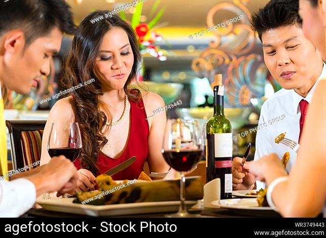 Two Asian Chinese Couples or friends or business people toasting during dinner or lunch in a elegant restaurant with red wine glasses