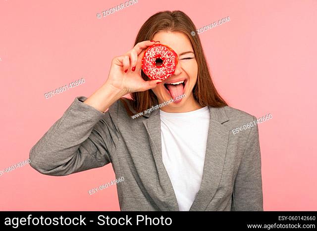 Health care and nutrition. Portrait of cheerful businesswoman in suit jacket looking through sweet doughnut, having fun with pastry