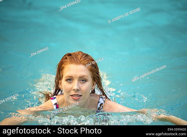A 27 year old redhead woman swimming in an outdoor pool
