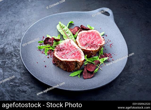 Fried dry aged beef fillet steak natural with vegetable fies and lettuce offered as close-up on a modern design plate