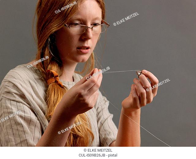 Young female designer threading a sewing needle