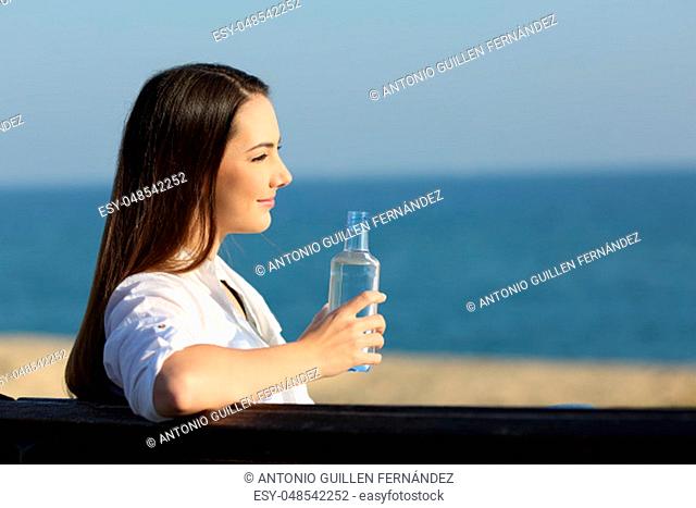 Smiley woman holding a water bottle and looking at horizon on the beach