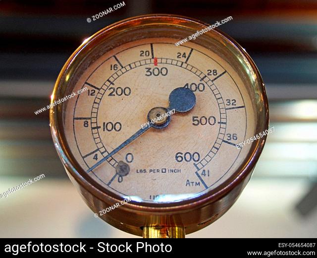 an old shiny brass round pressure gauge with a round dial marked in numbers and a black metal needle