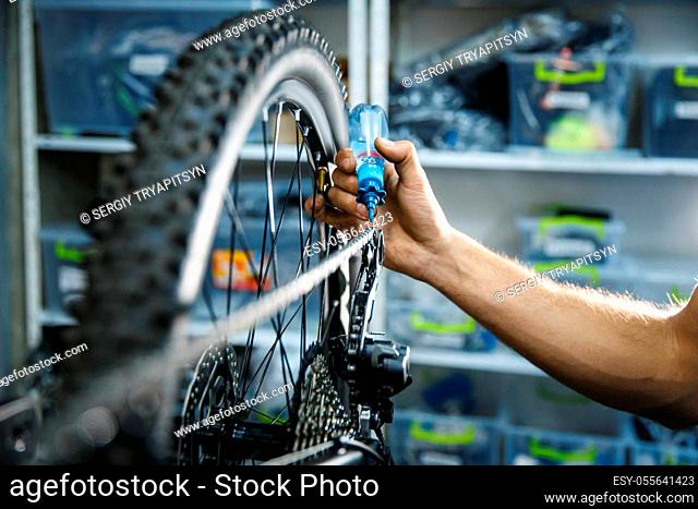 Bicycle assembly in workshop, man oiling the chain. Mechanic in uniform fix problems with cycle, professional bike repairing service