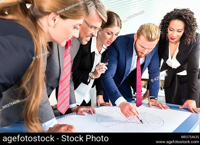 Group of business people are leaning over a desk and analyze graphs
