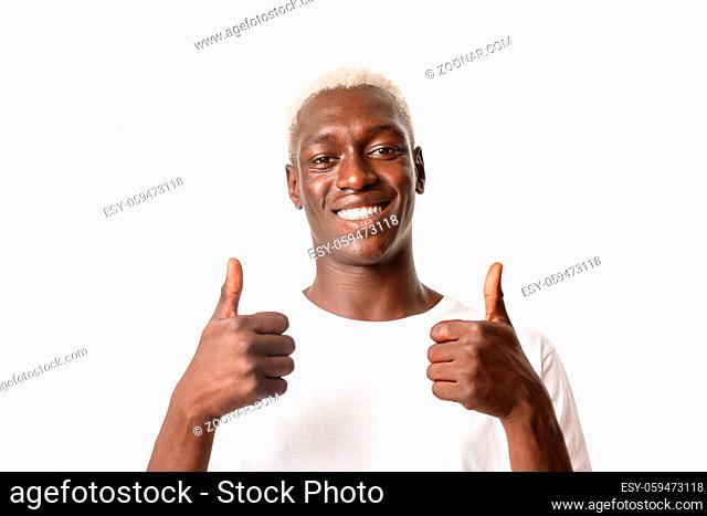 Close-up of pleased handsome african american blond guy smiling, showing thumbs-up in approval, like something, standing white background