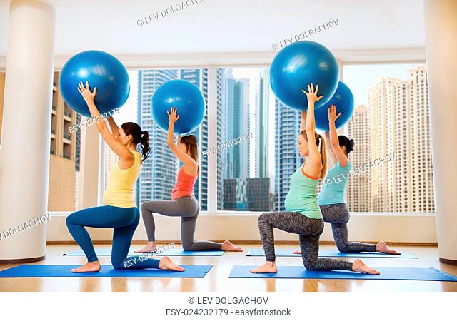 pregnancy, sport, fitness, people and healthy lifestyle concept - group of happy pregnant women exercising with ball in gym over city window view background