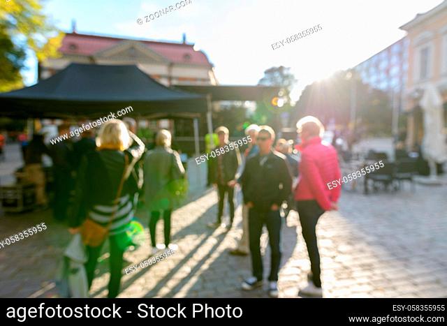 Portrait of defocused crowd of people looking busy in front of black canopies in the street on sunny day