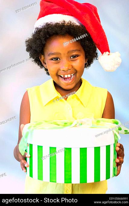 Close up portrait of happy african kid holding christmas gift boxes.Girl wearing red hat against light blue background