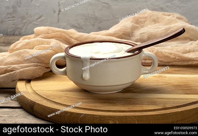 sour cream in a brown ceramic bowl with a wooden spoon on a wooden board background, fermented milk useful product