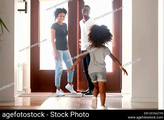 Happy little African American girl running to father returning, going back home after work, greetings, daughter with attractive smiling mother in hall welcome...