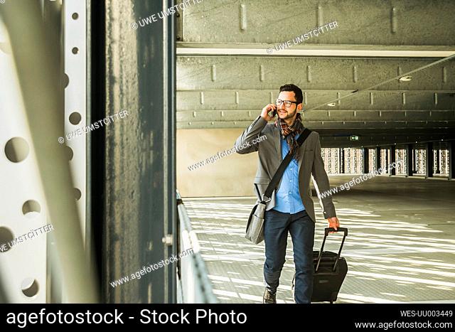 Young businessman walking in car park talking on cell phone