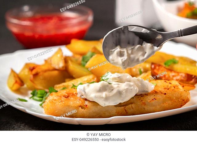 Fried fish and chips on a white plate on the kitchen table with tomato sauce, tartar sauce. Inpose on fish Tartar sauce - photo, image