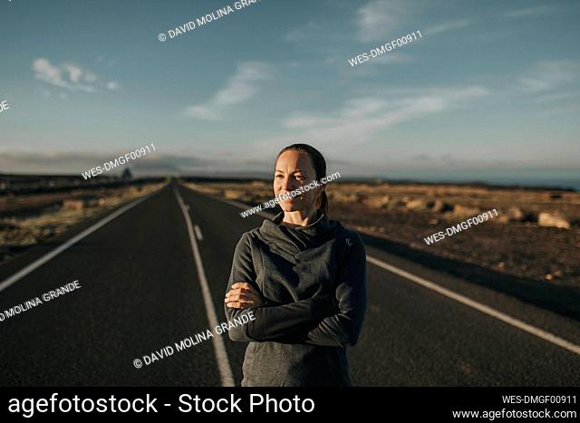 Thoughtful smiling woman standing on road in front of sky