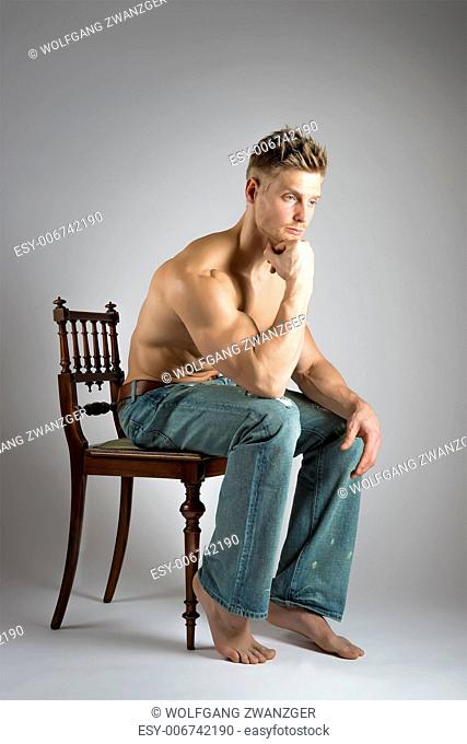 Blonde athlete with well trained muscles sitting on a chair and ponders