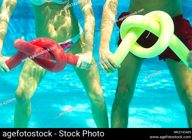Fitness - a young couple (man and woman) doing sports and gymnastics or water aerobics under water in swimming pool or spa with swim noodle
