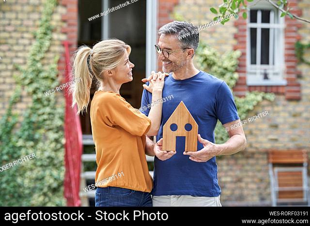 Happy man holding wooden house model by woman in back yard