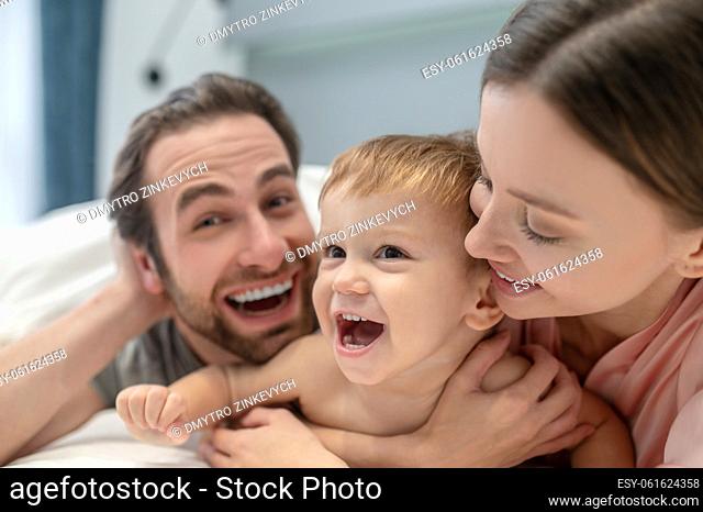 Cheerfulness. Close-up joyful faces of cute child woman and man with open mouth looking at camera lying on bed