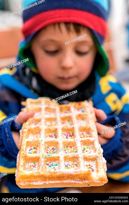 Little boy eating sweet waffle bought from a dessert stand in winter