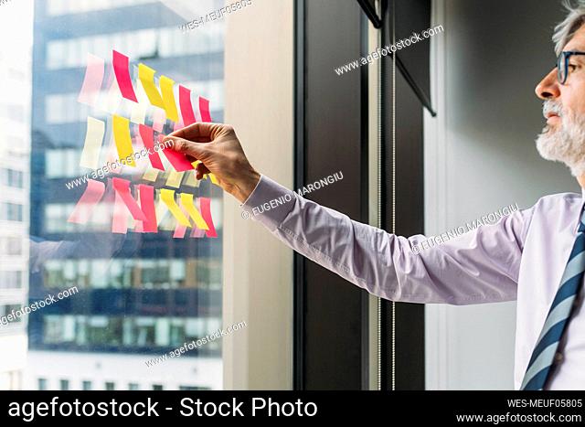 Mature businessman sticking adhesive notes on window in office