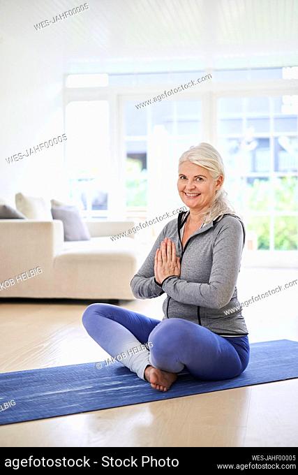Smiling mature woman with hands clasped meditating in living room