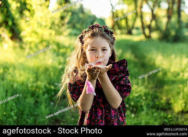 Playful girl with flower tiara blowing peony petal