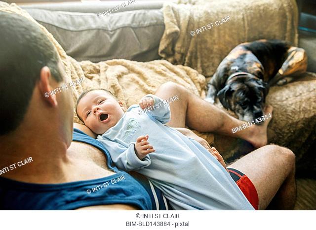 Caucasian father holding yawning baby boy in living room