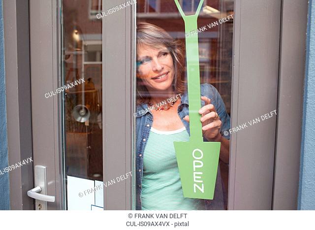 View through glass shop door of woman holding open sign