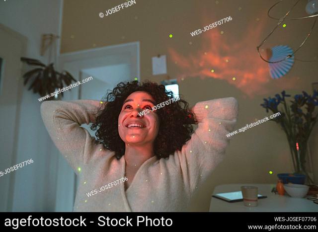 Happy woman with hands behind head looking at astro light effects in room