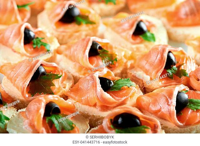 Cropped clos up of buttered canapes with smoked salmon decorated with black olives eating food tasty meny serving delicacy gourmet cafe restaurant appetite...