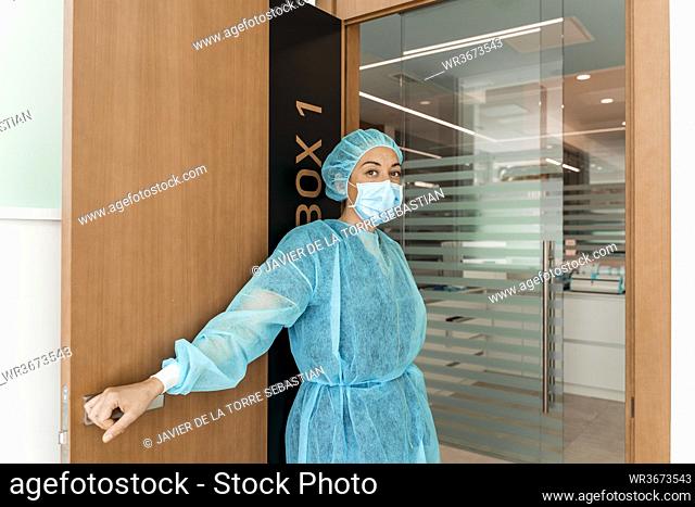 Female dentist in protective wear standing at doorway