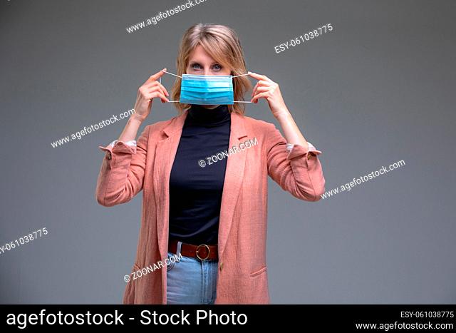 Head portrait attractive blond woman hold her surgical mask protecting from COVID19 or corona virus. Personal care during pandemic infectious