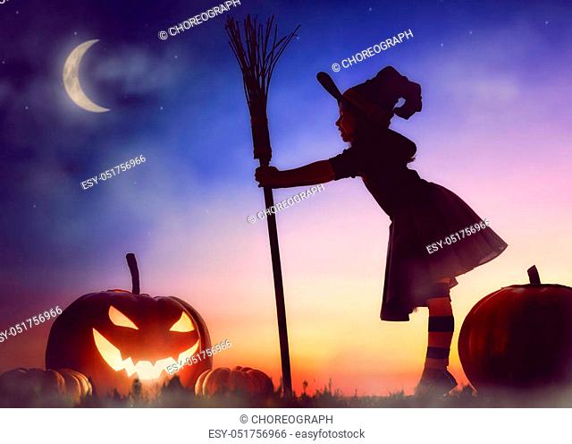 Happy Halloween! Cute little witch with a big pumpkin. Beautiful young child girl in witch costume outdoors