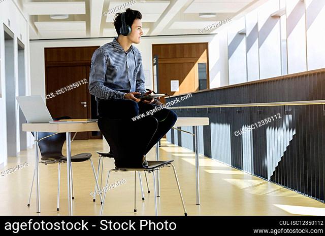 Germany, Bavaria, Munich, Young man with headphones sitting on desk