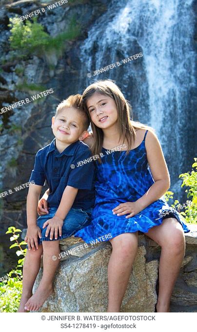 A young brother and sister sitting together outdoors