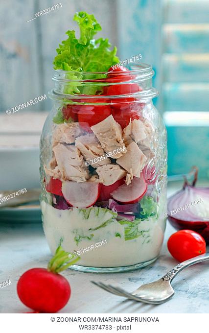 Salad with chicken and fresh vegetables in a glass jar on an old kitchen table, selective focus