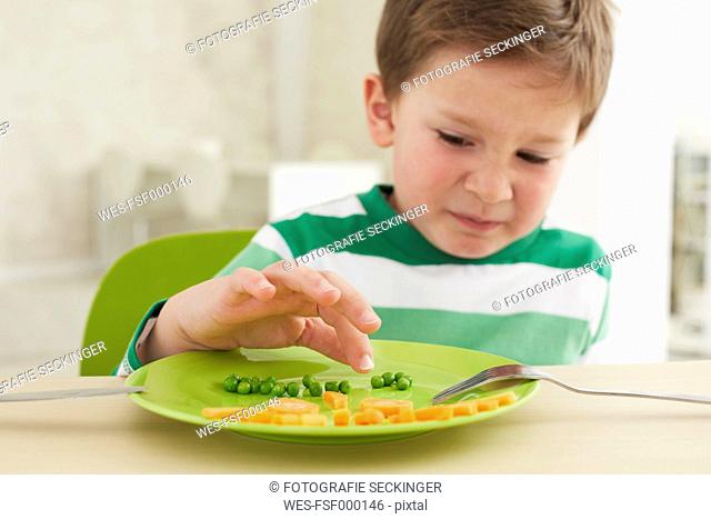 Germany, Munich , Boy eating peas and carrots showing anthropomorphic face