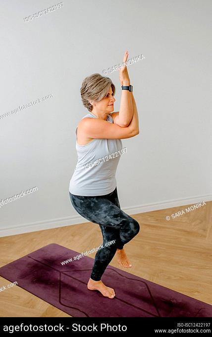 Woman in garudasana on yoga mat at home