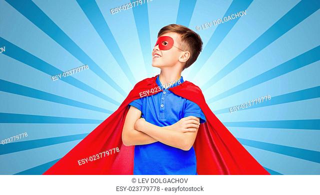 carnival, childhood, power, gesture and people concept - happy boy in red super hero cape and mask over blue burst rays background