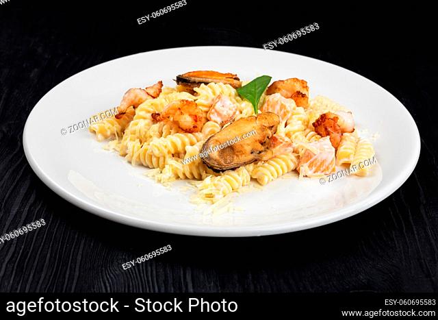 Seafood Pasta with mussels salmon and shrimps with basil in white plate on black wooden background