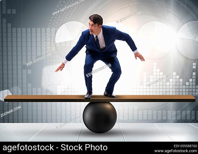 The businessman trying to balance on ball and seesaw