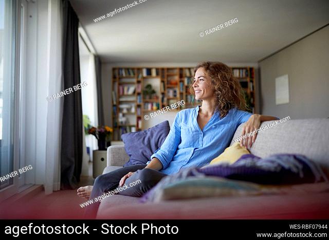 Smiling woman looking away while sitting on sofa at home